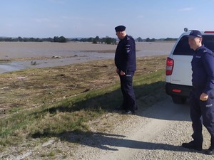 zdjęcie przedstawia komendanta z policjantem na tle zbiornika wodnego oraz samochodu