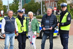 zdjęcie kolorowe przedstawia policjantów wraz z uczestnikami akcji na tle radiowozu