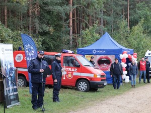 Na zdjęciu lektor w trakcie zapowiadania przebiegu Ogólnopolskich Mistrzostw Policji w XXI Biegu Przełajowym im. Grzegorza Załogi. W tle widać osoby zaangażowane w organizację przedsięwzięcia.