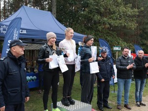 Zdjęcie pamiątkowe, na którym widać stojące na podium laureatki jednej z kategorii w towarzystwie Naczelnika Wydziału Doboru i Szkolenia KWP w Katowicach oraz gości honorowych.