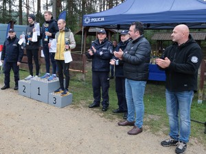 Zdjęcie pamiątkowe, na którym widać stojące na podium lauretów jednej z kategorii w towarzystwie Naczelnika Wydziału Doboru i Szkolenia KWP w Katowicach oraz gości honorowych.