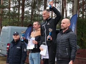 Zdjęcie pamiątkowe, na którym widać stojących na podium laureatów w męskiej kategorii biegu w towarzystwie Naczelnika Wydziału Doboru i Szkolenia KWP w Katowicach.