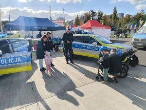 Na zdjęciu widać dzieci z opiekunami przy policjancie stojącym obok radiowozu