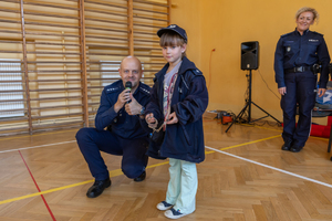 Na zdjęciu policjant z mikrofonem i dziewczynka mundurze policjanta.