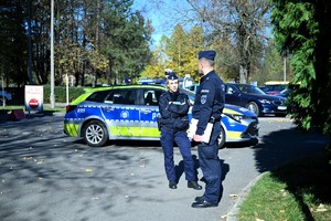 Zdjęcie przedstawia policjanta, policjantkę oraz radiowóz w tle