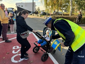 Na zdjęciu policjant wręcza chorągiewkę dziecku w wózku