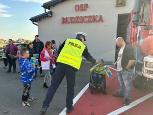 Na zdjęciu policjant wręcza chorągiewkę dziecku na wózku