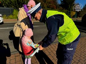 Na zdjęciu policjant zakładający opaskę odblaskową dziecku.