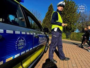 Na zdjęciu policjant ruchu drogowego trzymający w ręku opaski odblaskowe.