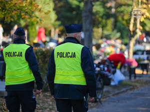 Na zdjęciu dwójka policjantów patrolujących cmentarne alejki.