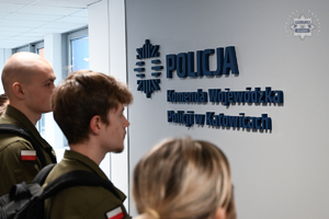 Na zdjęciu uczniowie spoglądają na logo Komendy Wojewódzkiej Policji w Katowicach.