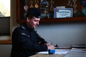 Na zdjęciu umundurowany funkcjonariusz Policji podpisujący dokumenty