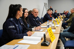 na zdjęciu policjanci i osoby siedzące wspólnie przy stołach