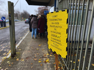 na zdjęciu usytuowana przed wejściem na teren wojewódzkiej komendy tabliczka żółtego koloru, na niej napis Punkt stawiennictwa dla osób zgłaszających się na ćwiczenie EGIDA 24 w Komendzie Wojewódzkiej Policji w Katowicach, za tabliczką widoczne osoby