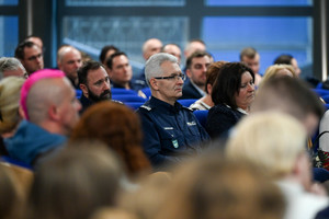 na zdjęciu siedzące na krzesłach osoby i policjanci, pośród nich komendant wojewódzki.