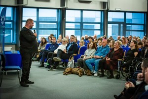 na zdjęciu mężczyzna przemawiający do mikrofonu przed osobami zgromadzonymi w sali konferencyjnej.