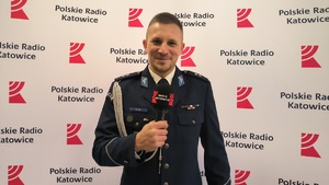 na zdjęciu policjant z mikrofonem w dłoni, za nim ścianka z napisem Polskie Radio Katowice.