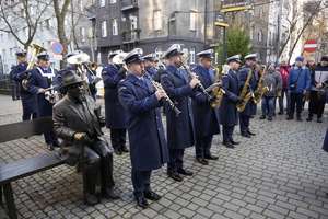 na zdjęciu mundurowi ustawieni w kilku rzędach,  grający na instrumentach obok nich zgromadzone osoby.