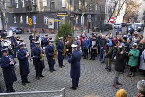 na zdjęciu mundurowi ustawieni w kilku rzędach,  grający na instrumentach obok nich zgromadzone osoby.