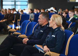 na zdjęciu policjantka, policjant i osoby siedzące na krzesłach w sali