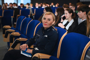 na zdjęciu policjantka, za nią osoby siedzące na krzesłach w sali