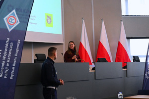 na zdjęciu policjant odwrócony w stronę młodej kobiety trzymającej w dłoniach mikrofon