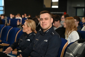 na zdjęciu policjant i policjantka oraz osoby siedzące na krzesłach w auli