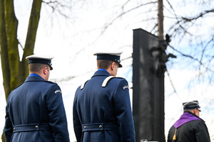 Na zdjęciu policjanci w mundurze galowym na tle Pomnika upamiętniającego zmarłych w katastrofie MTK