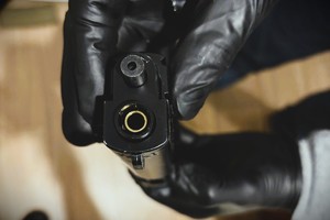 na zdjęciu dłonie osoby trzymające pistolet wylotem lufy w kierunku obiektywu