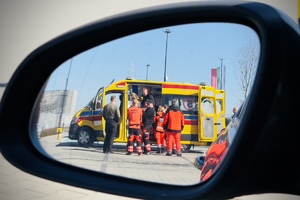 Zdjęcie lusterka samochodowego, w którym widać karetkę pogotowia wraz z ratownikami