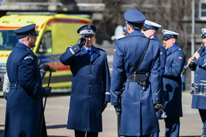 dowódca uroczystości stoi tyłem przed nim komendant wojewódzki obok policjant który trzyma mikrofon zdjęcie prezentuje złożenie meldunku komendantowi wojewódzkiemu