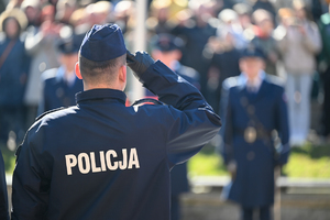 zbliżenie i ostrość na policjanta który stoi tyłem i oddaje honor w tle mniej widoczni uczestnicy uroczystości