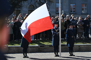 zbliżenie na flagę państwową w tle uczestnicy uroczystości