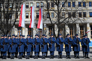 kompania honorowa stoi w szyku za nią budynek oraz dwie zawieszone flagi państwowe