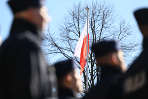 na pierwszym planie mało ostrzy policjanci stojący w rzędach za nimi dobrze widoczna flaga państwowa