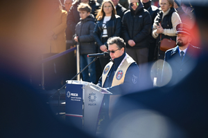 na pierwszym planie mało widoczni tyłem stoją policjanci za nimi dobrze widoczny kapelan policji w tle zaproszeni goście