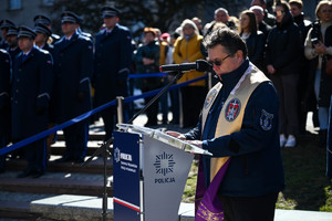 zdjęcie kapelana policji przy mównicy w tle za nim policjanci i zaproszeni goście