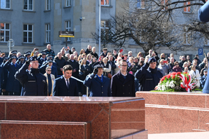 na pierwszym planie bryła pomnika za nią delegacja oddająca honor widoczna wiązanka w tle zaproszeni goście