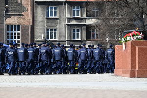 fragment pomnika z wiązanką obok maszerujący policjanci