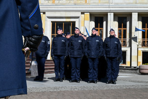 zbliżenie na dłoń trzymającą szablę w tle mniej widoczni policjanci składający meldunek