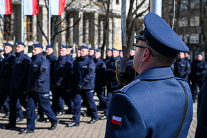 zbliżenie na fragment sylwetki policjanta z kompanii honorowej który trzyma podniesioną szablę w tle maszerujący policjanci