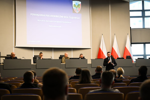 Zdjęcie przedstawia mężczyznę w garniturze oraz uczestników szkolenia.