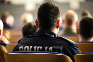Zdjęcie przedstawia umundurowanego policjanta siedzącego w sali podczas szkolenia.