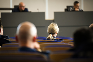 Zdjęcie przedstawia umundurowaną policjantkę siedzącą w sali podczas szkolenia.