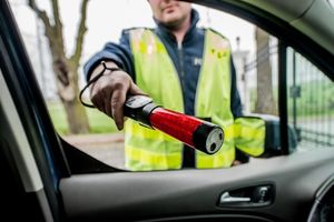 Zdjęcie przedstawia umundurowanego policjanta wydziału ruchu drogowego przeprowadzającego kontrolę trzeźwości.