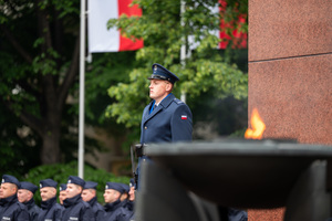 Na zdjęciu widoczny policjant w umundurowaniu galowym, flaga Polski , płomień i ślubujący policjanci.