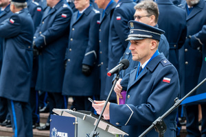 Grafika przedstawia oficera Policji stojącego za mównicą.