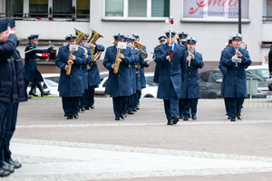 Grafika przedstawia umundurowaną orkiestrę Policji na Placu Chrobrego w Katowicach.