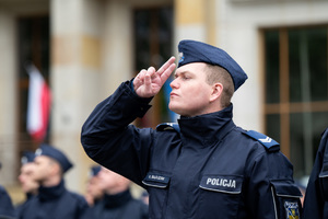 Grafika przedstawia starszego sierżanta policji w umundurowaniu ćwiczebnym oddającego honor.