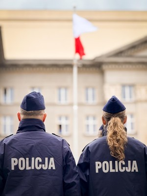 Na zdjęciu policjant i policjantka stojący tyłem.